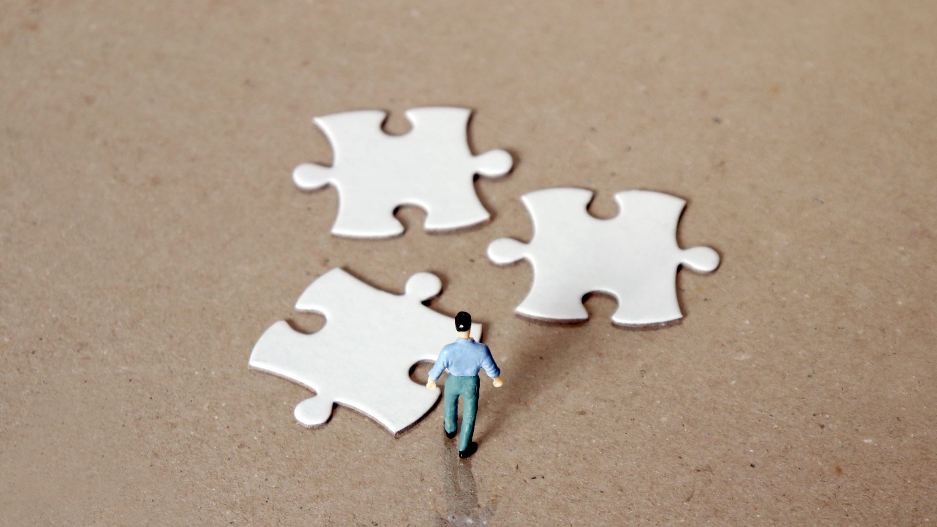 A miniature man staring down three pieces of the puzzle. A miniature man staring down three pieces of the puzzle.